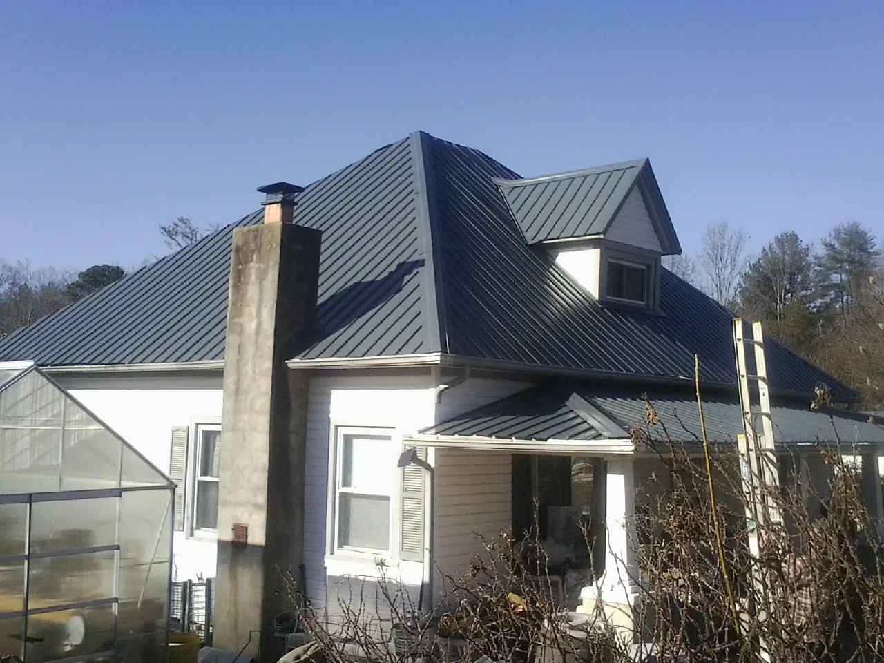 Dark blue standing seam metal roof on a white farmhouse with dormer — Slate & Tile Roof Repair by Roofing Brothers in Nixon