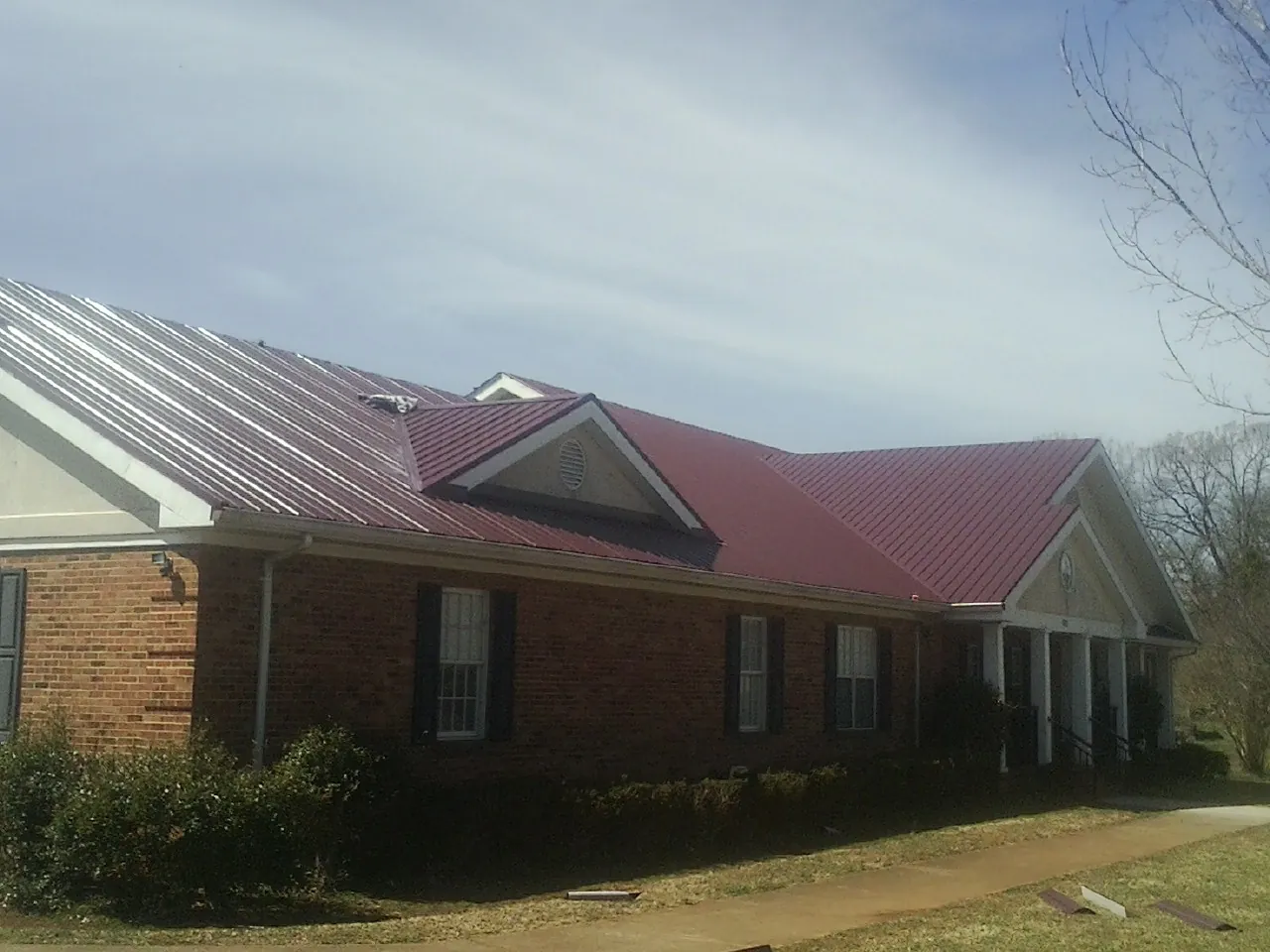 Red metal roof with gabled entries on a long brick building, from a Hail Damage Roof Repair job in Nixon
