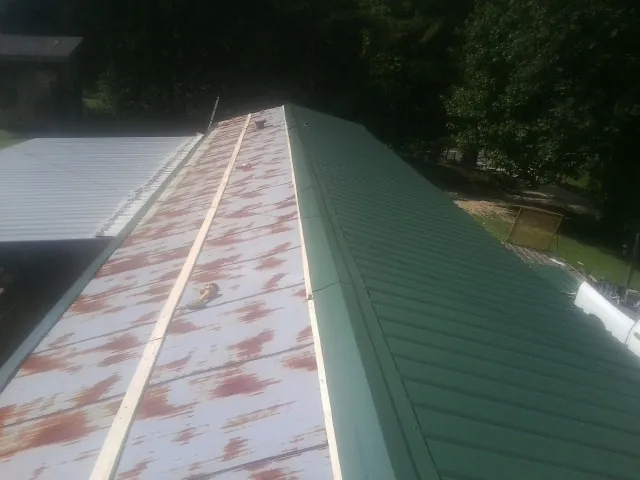 Old rusted panels beside newly installed green metal roofing — Wind Damage Roof Repair by Roofing Brothers in Nixon