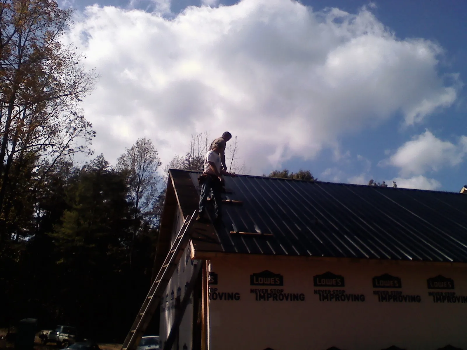 Roofer fastening dark metal panels high against a cloudy sky, from a Roof Inspection job in Nixon