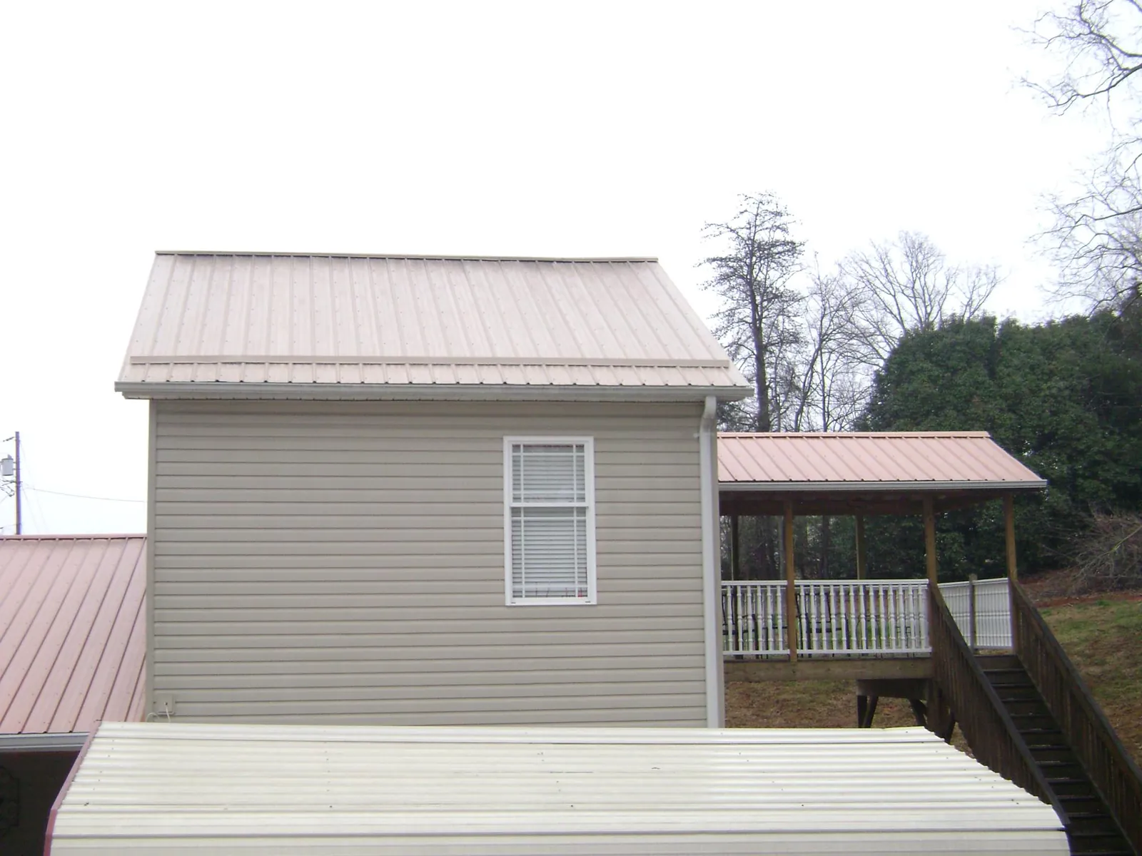 Tan metal roofs on a two story addition and attached porch, from a Roof Replacement job in Nixon